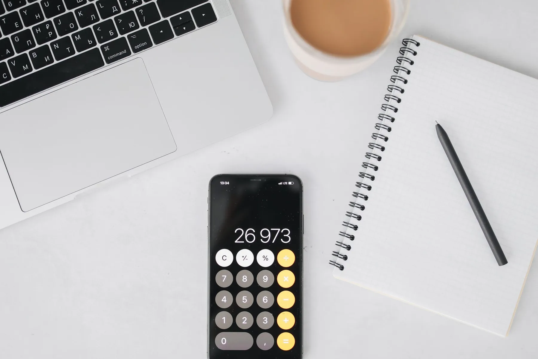 A phone calculator, a notebook and a laptop on a desk