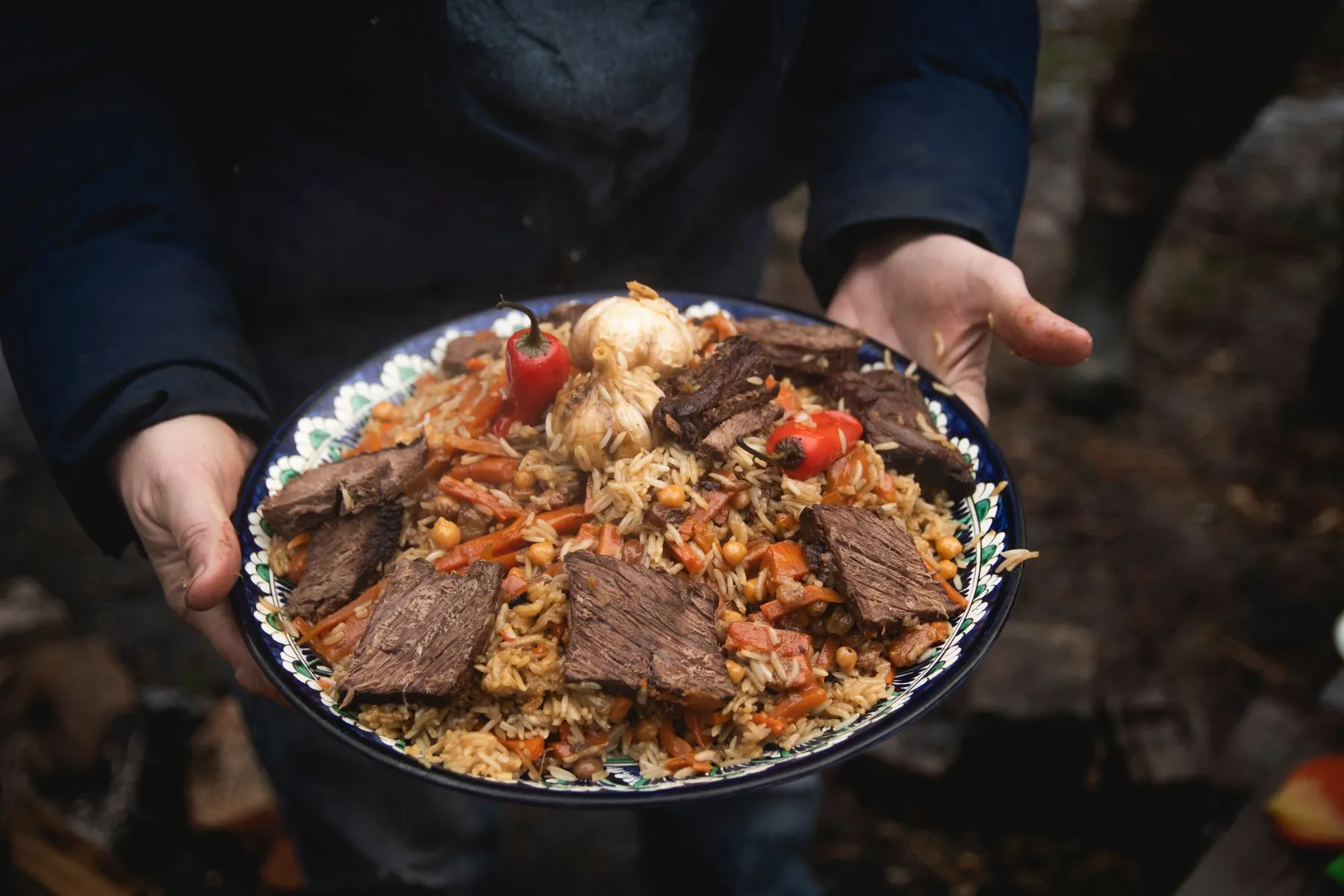 A dish of plov with meat, held in both hands