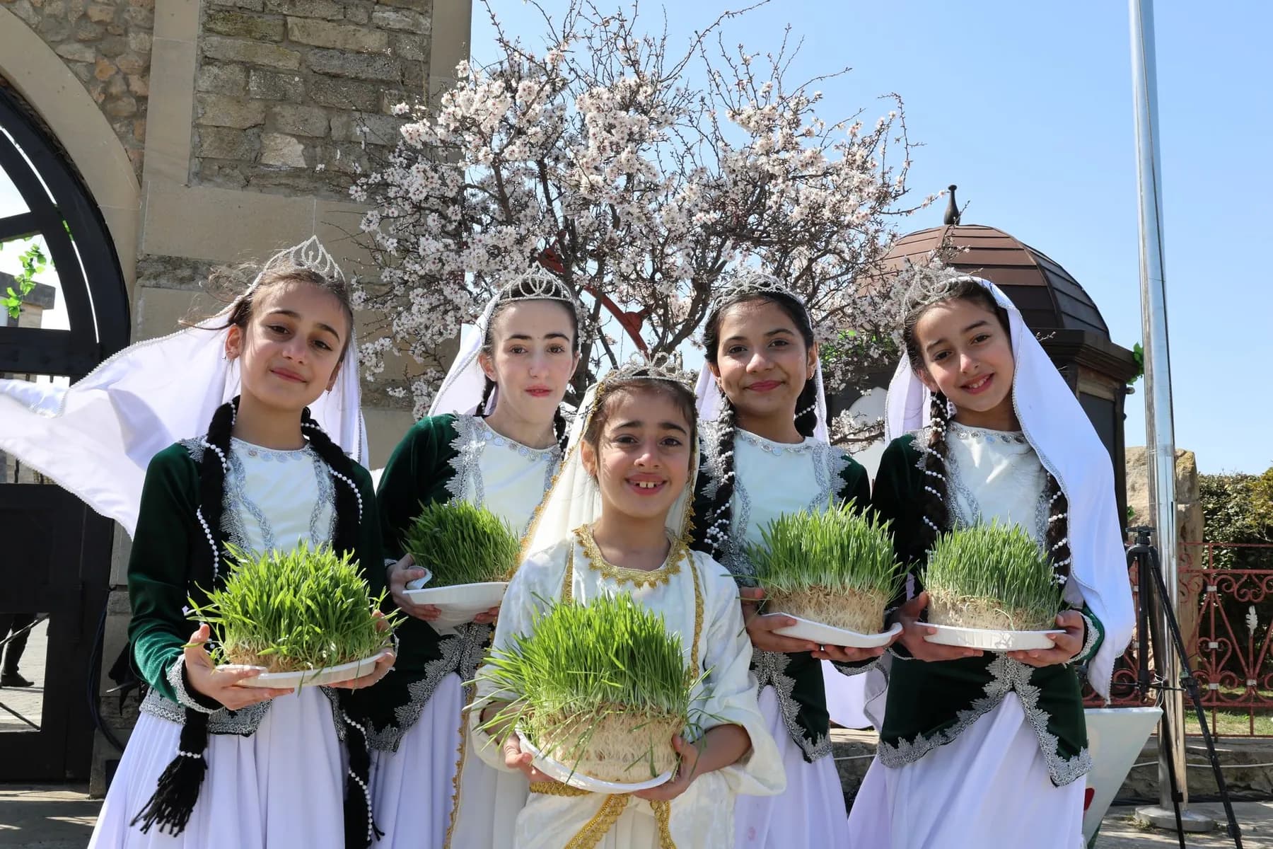 Girls in traditional dress holding sprouted wheat for Navruz