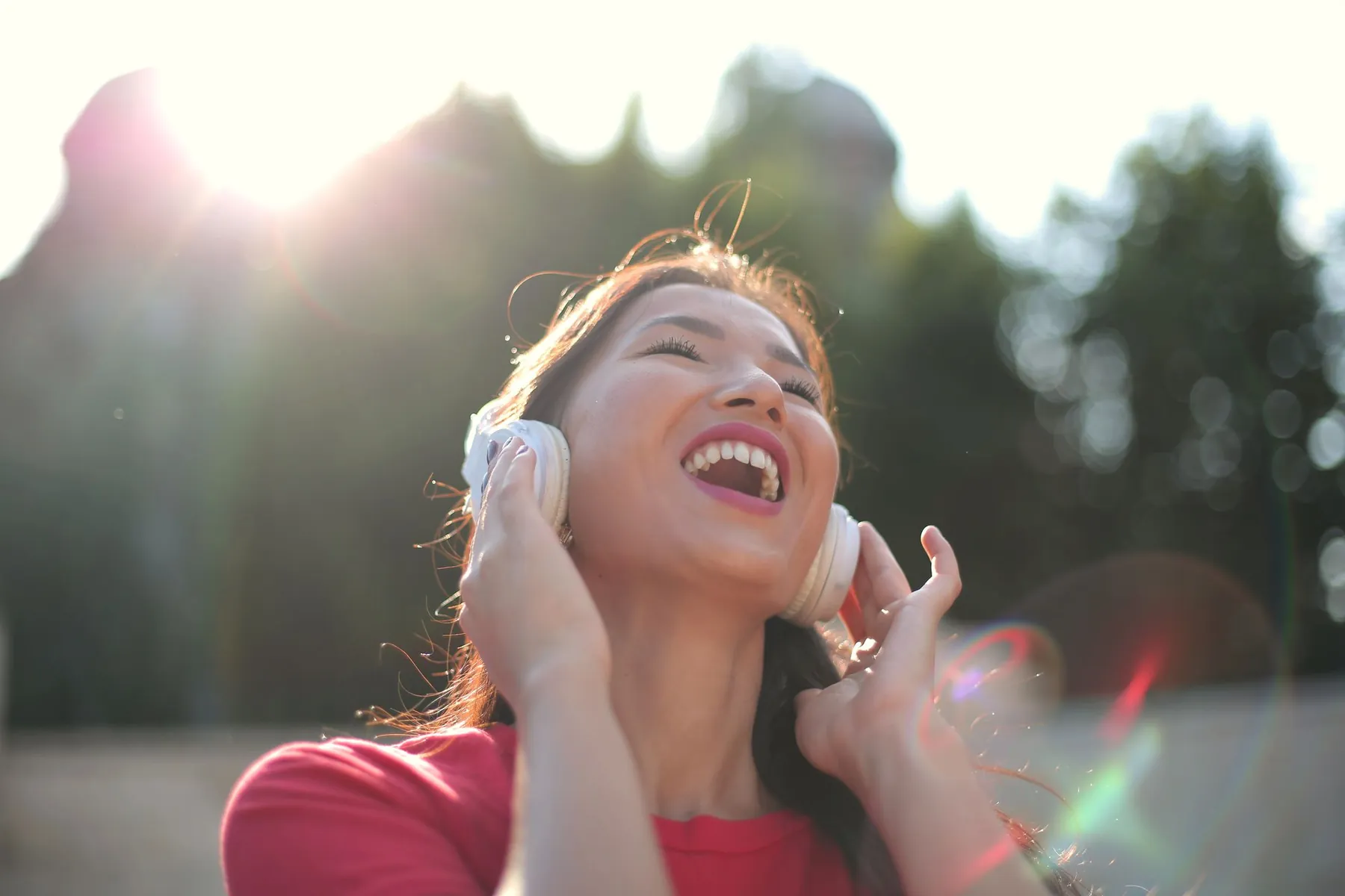 A woman laughing as she listens to music in the sun