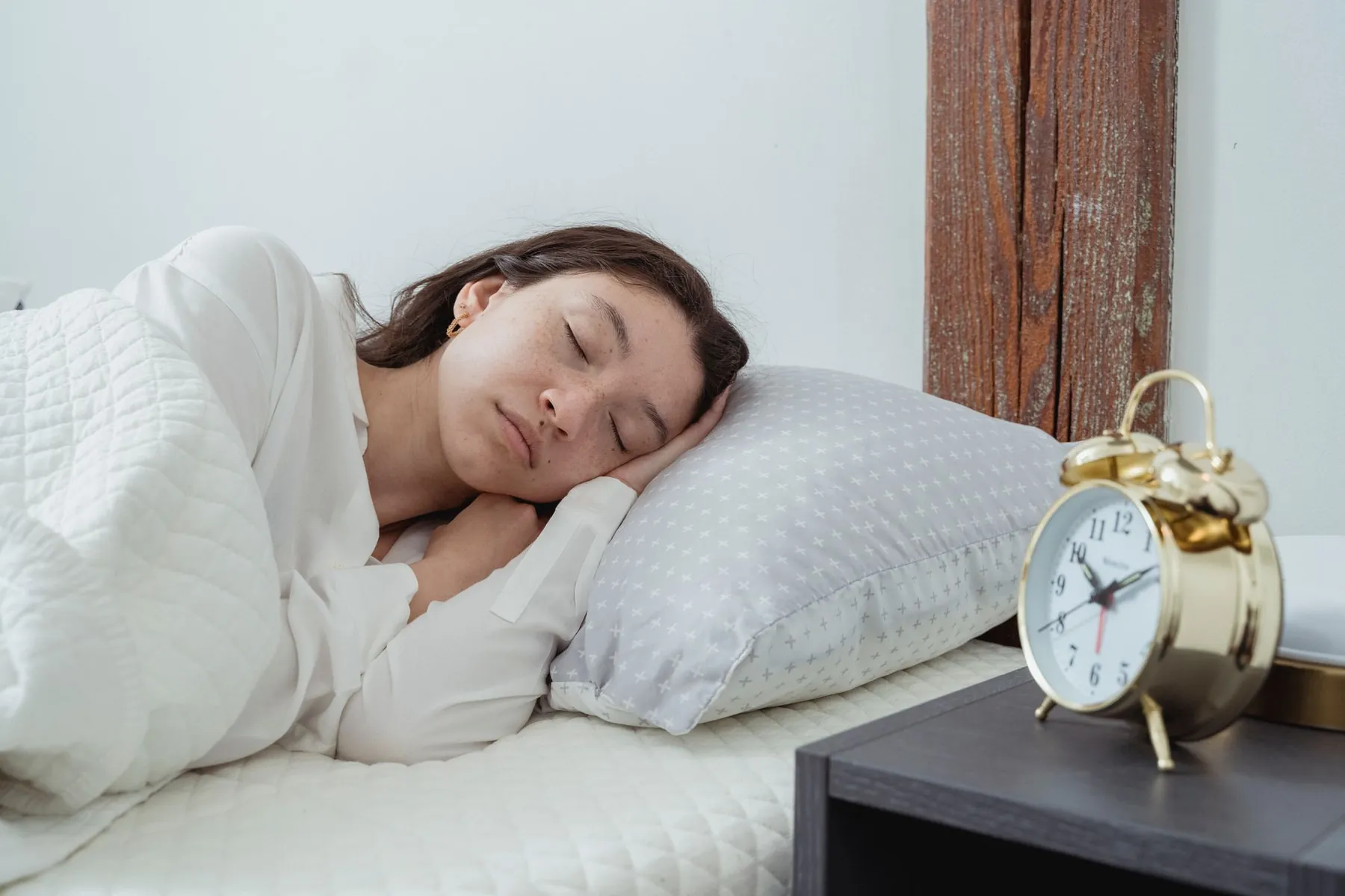 A woman asleep with an alarm clock beside the bed