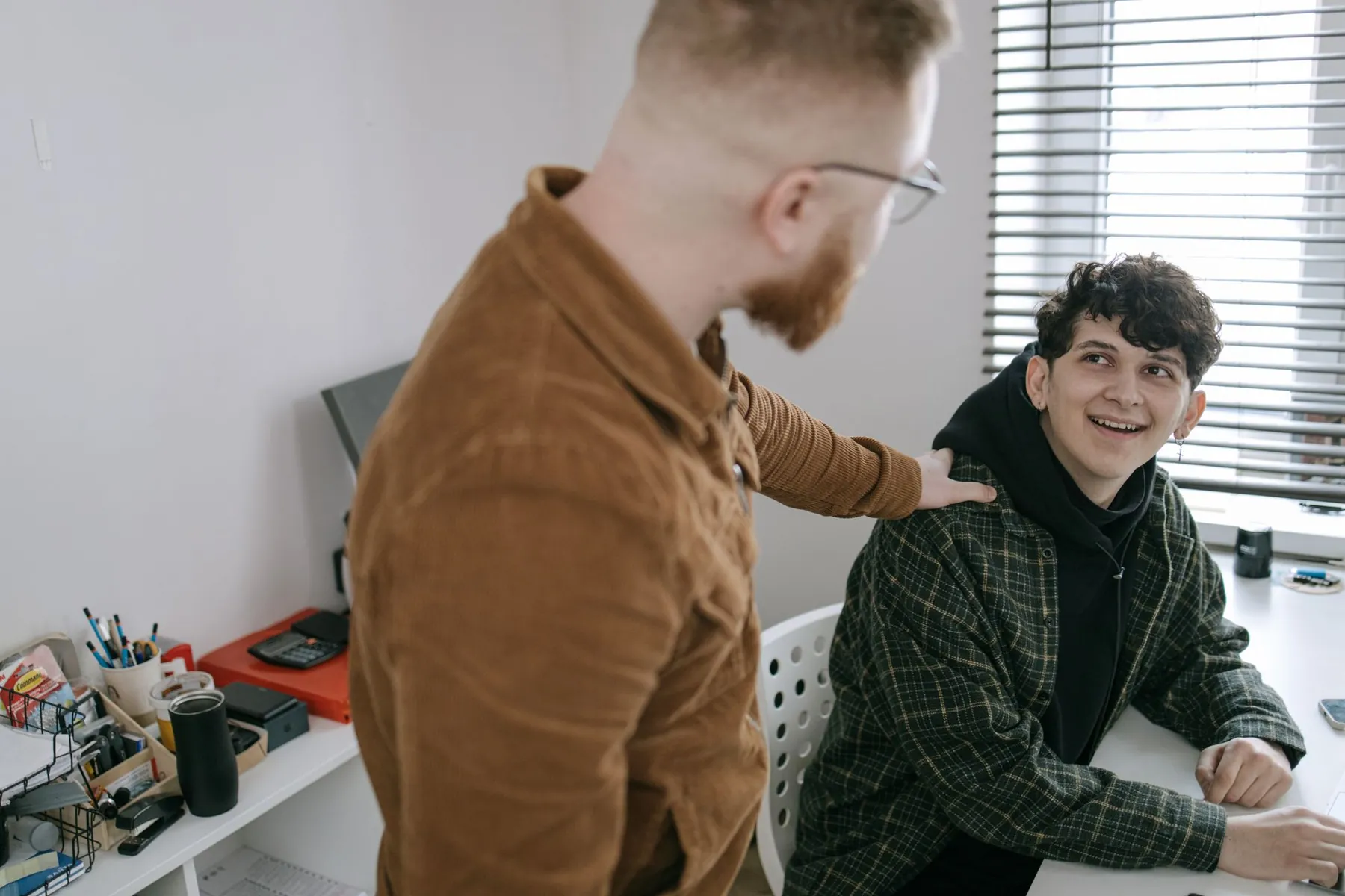 A man with a hand on a smiling teenager's shoulder, talking with him
