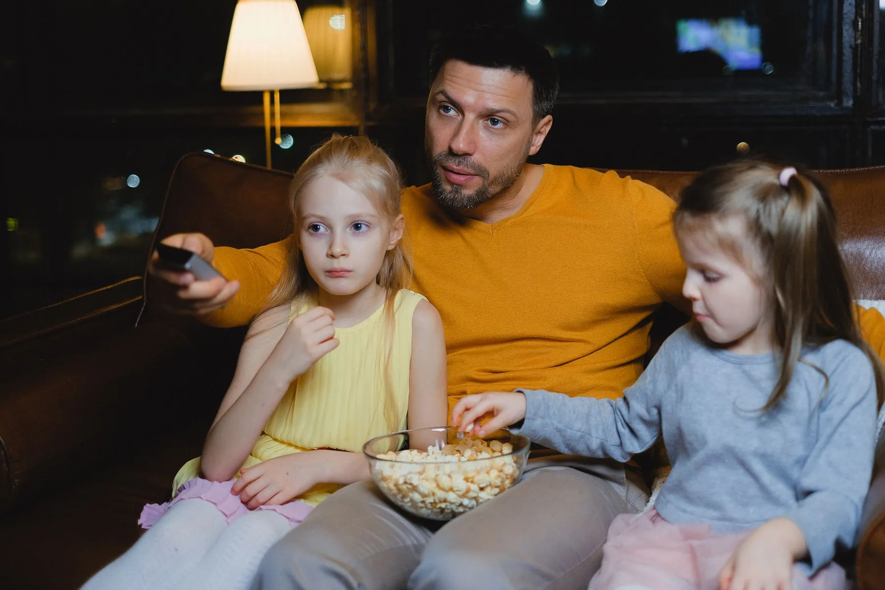 A father and his daughters watching a film with popcorn