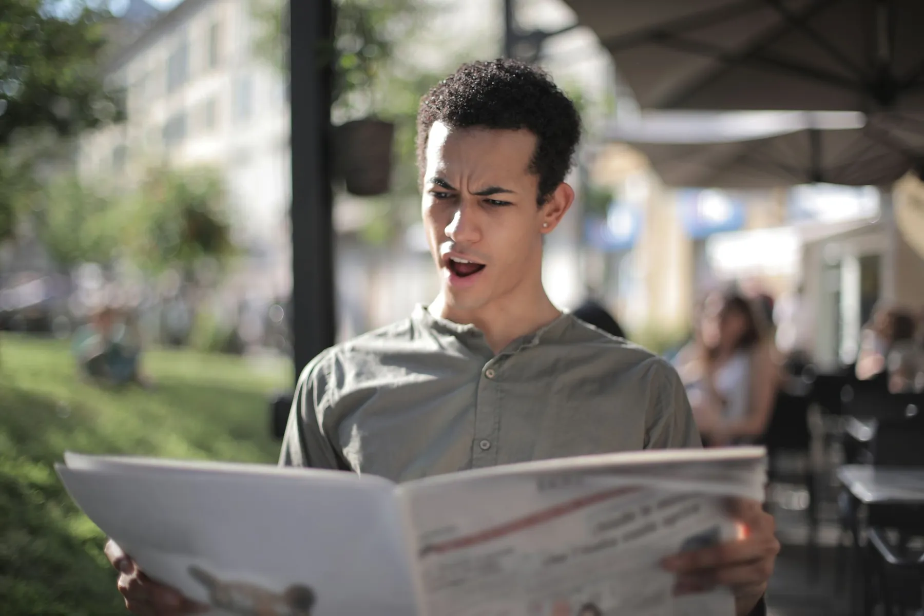 A young man looking surprised as he reads a newspaper at a café