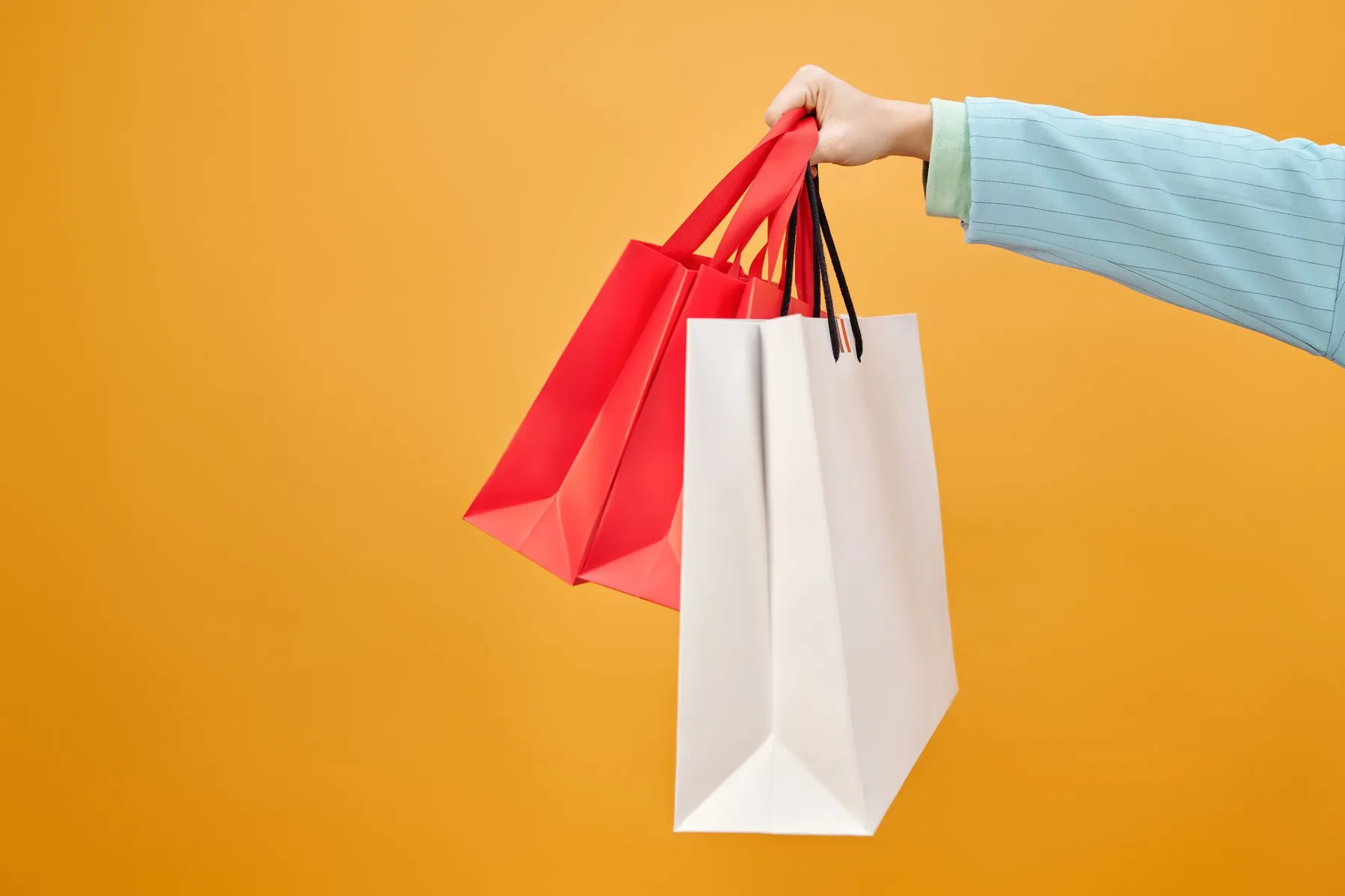 A hand holding shopping bags against an orange background